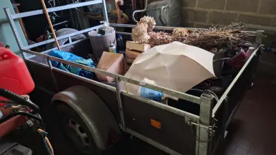 Enkelassige aanhangwagen met metalen zijborden gevuld met diverse spullen waaronder een parasol en snoeiafval pas op 1 band is plat – kavel bij Goeiendeal, Houthalen-Helchteren