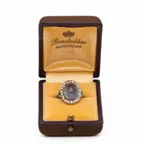 Geelgouden en platina belle-époque-entouragering, centraal bezet met een ovale bolcabochon geslepen grijs-lavendelblauwe saffier met lichte chatoya… – kavel bij Venduhuis De Eland