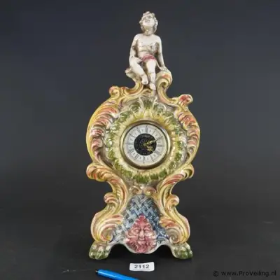Antieke mantelklok in rococostijl met een prachtig handbeschilderd keramieken uiterlijk en een sierlijk zittend putto-figuurtje bovenop – kavel bij ProVeiling, Wageningen