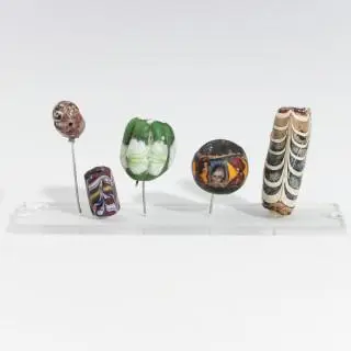 A Roman-Egyptian glass face bead, 1st century BCE, a Roman glass head, ca. 1st century CE and three Roman polychrome colored glass beads, ca. 1st c… – kavel bij Veilinggebouw De Zw