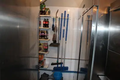 Schoonmaakartikelen waaronder bezem en trekker aan wandbeugel en in krat – kavel bij HNVI, Eindhoven